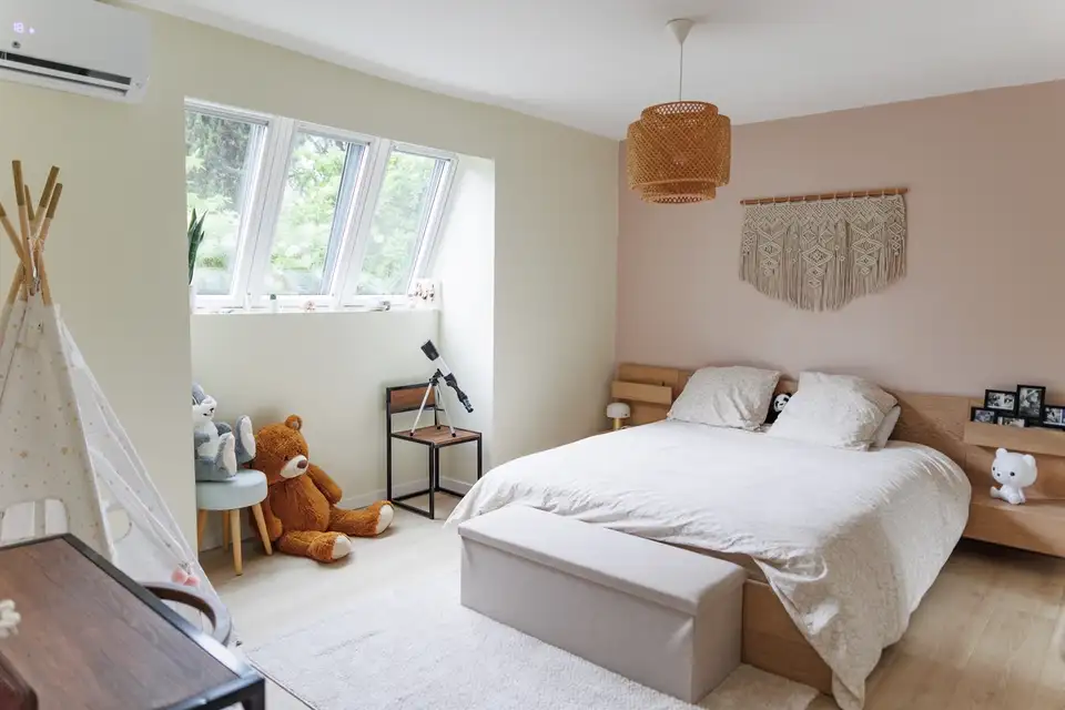 Une chambre confortable avec un mur d'accent rose doux, un grand lit et trois fenêtres de toit VELUX apportant de la lumière naturelle.