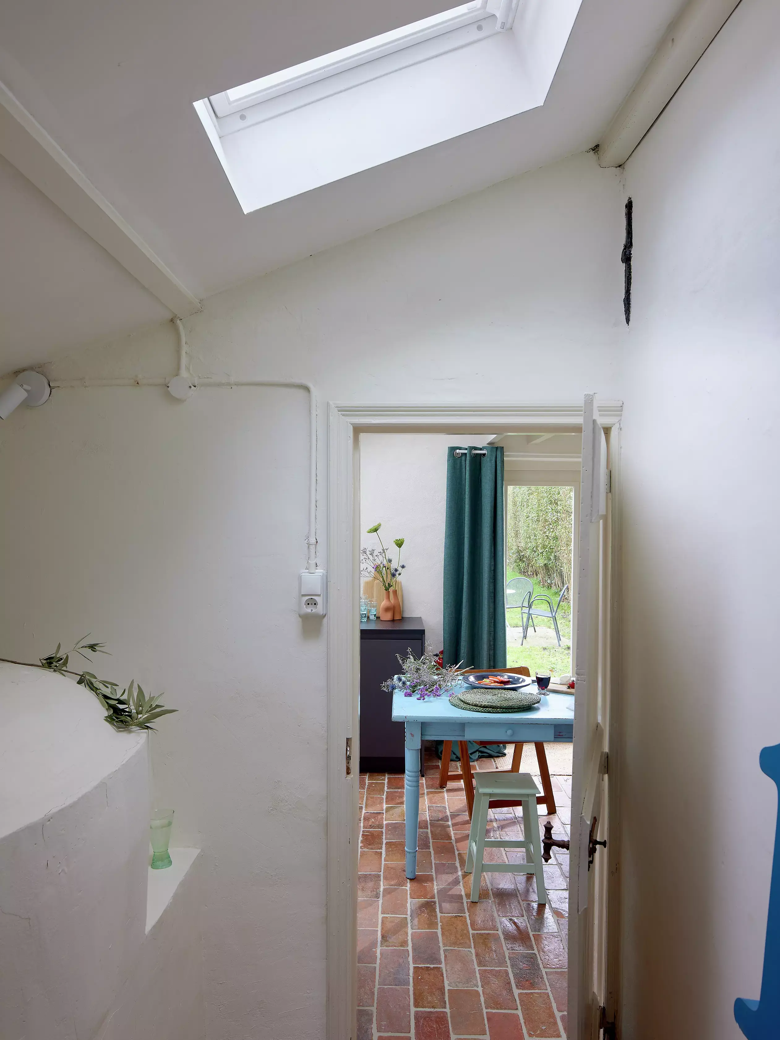 Espace salle à manger lumineux avec fenêtre de toit VELUX, carreaux en terre cuite et table bleue.