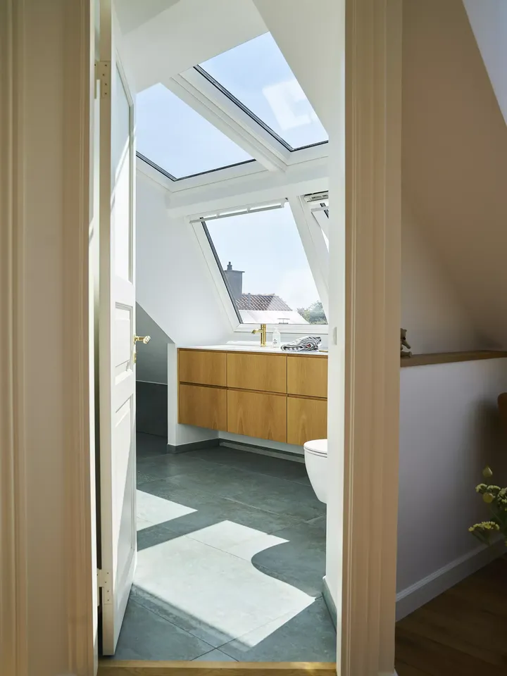 Modernes Badezimmer mit natürlichem Licht von VELUX Dachflächenfenster, hölzerner Waschtisch und zeitgenössisches Design.