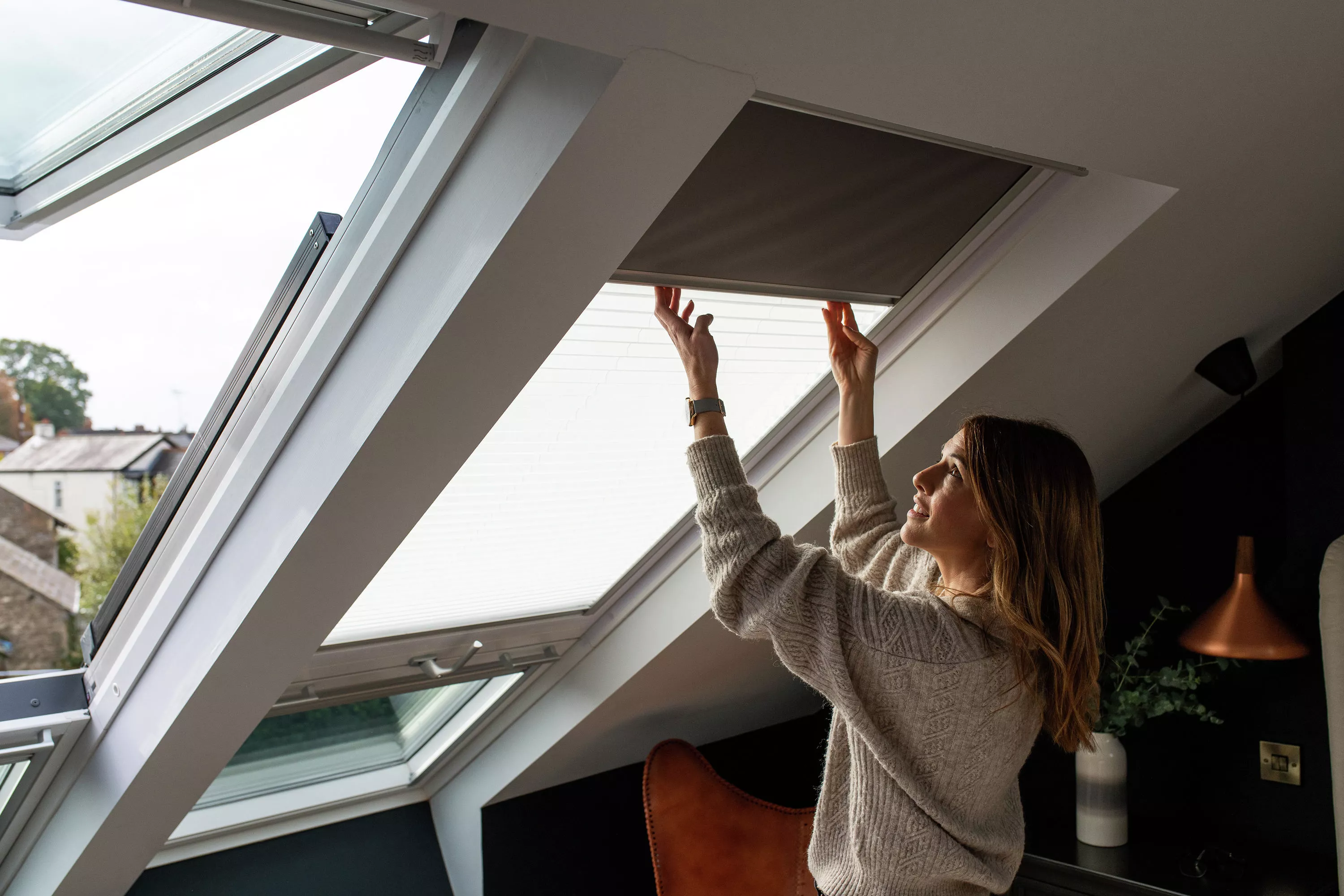 Person adjusting the blind of a VELUX skylight in a well-lit, modern loft room.