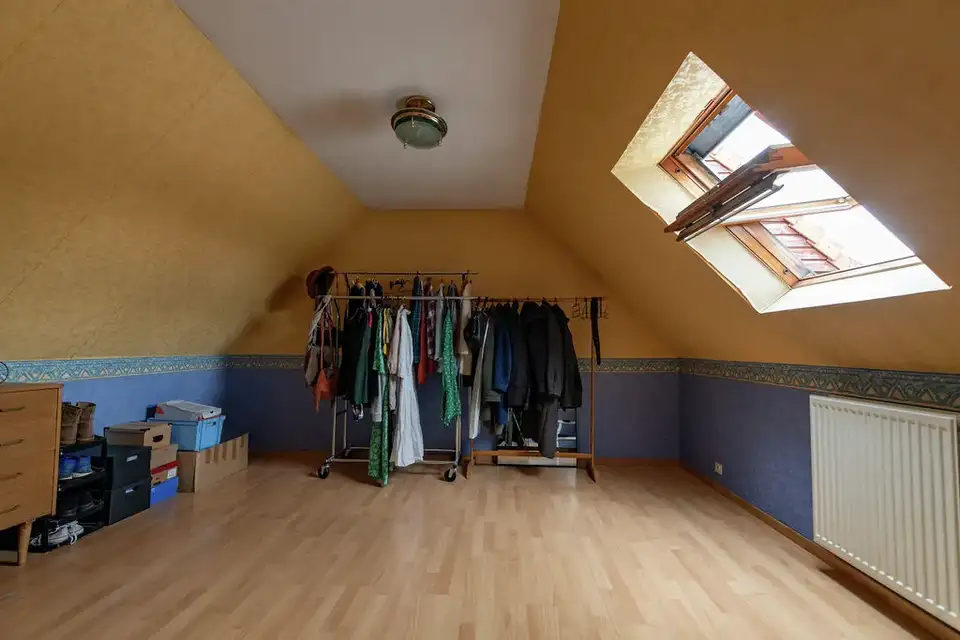 Grenier sous les toits avant rénovation, avec déco vieillissante et une seule fenêtre de toit vétuste