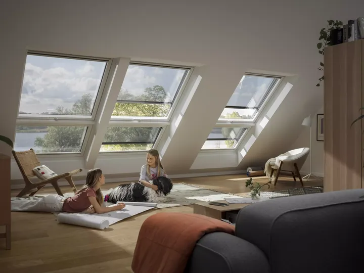 Kinder spielen in einem hellen Dachbodenraum mit VELUX Dachflächenfenstern mit Blick aufs Grüne.