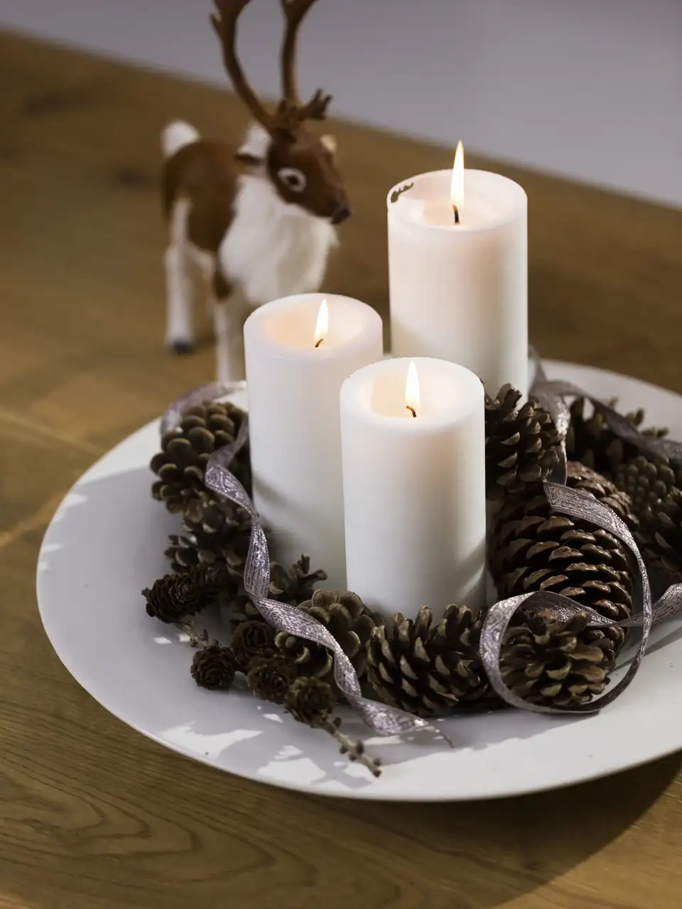 Centrotavola natalizio con candele bianche, pigne e nastri su tavolo in legno, decorazione ispirata alla natura.