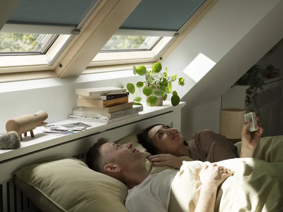 Coppia nel letto matrimoniale abbassa le tende interne con il telecomando per le finestre e gli accessori elettrici.