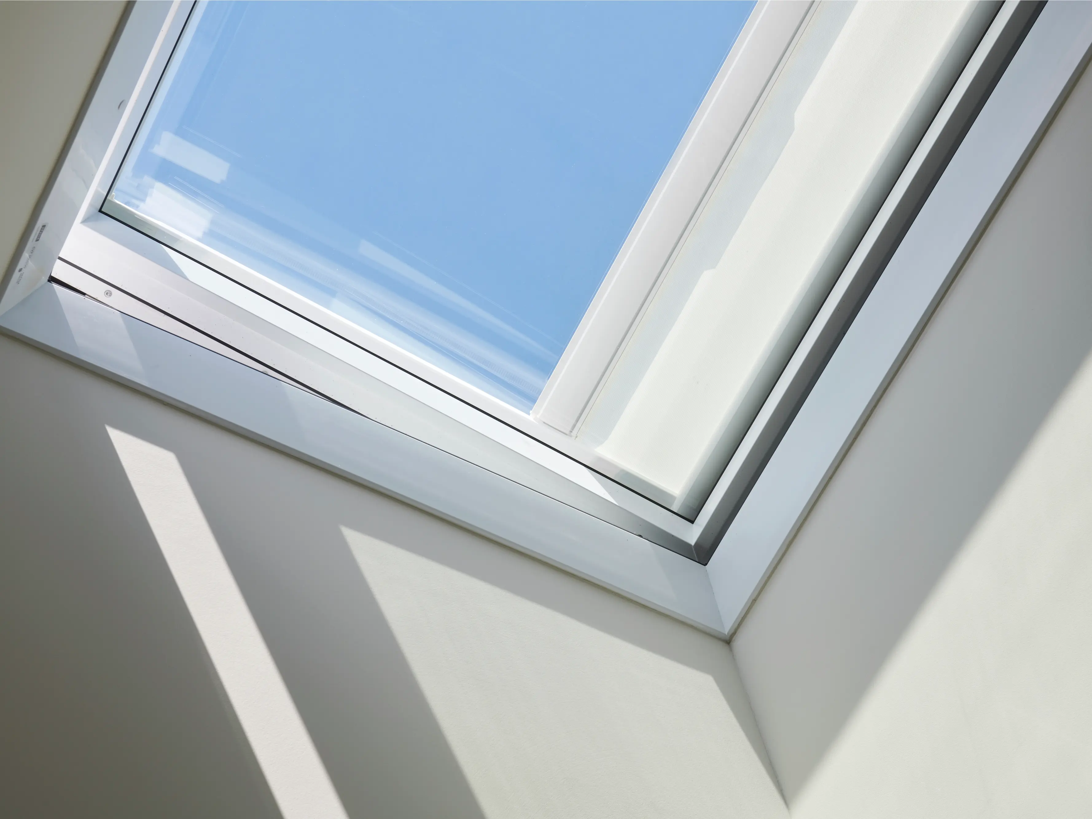 Fenêtre de toit minimaliste VELUX laissant entrer la lumière naturelle et la vue du ciel bleu.