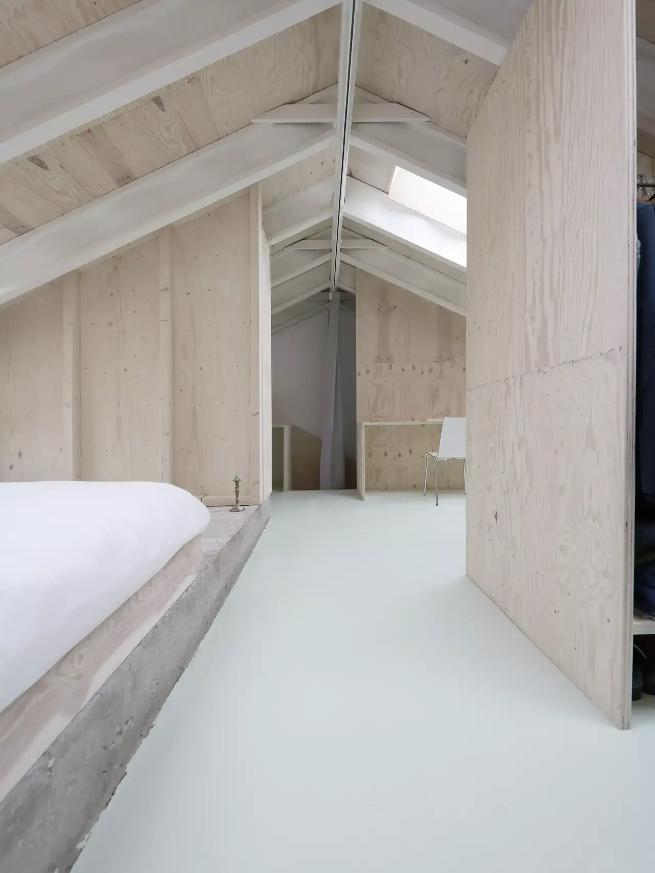 Intérieur avec plafond incliné en bois et deux puits de lumière. À gauche, une télévision murale affichant une image abstraite. En dessous, un poêle à bois noir. À droite, un bureau avec plusieurs moniteurs et des haut-parleurs. Éclairage ambiant rose-violet, créant une atmosphère moderne et cosy.