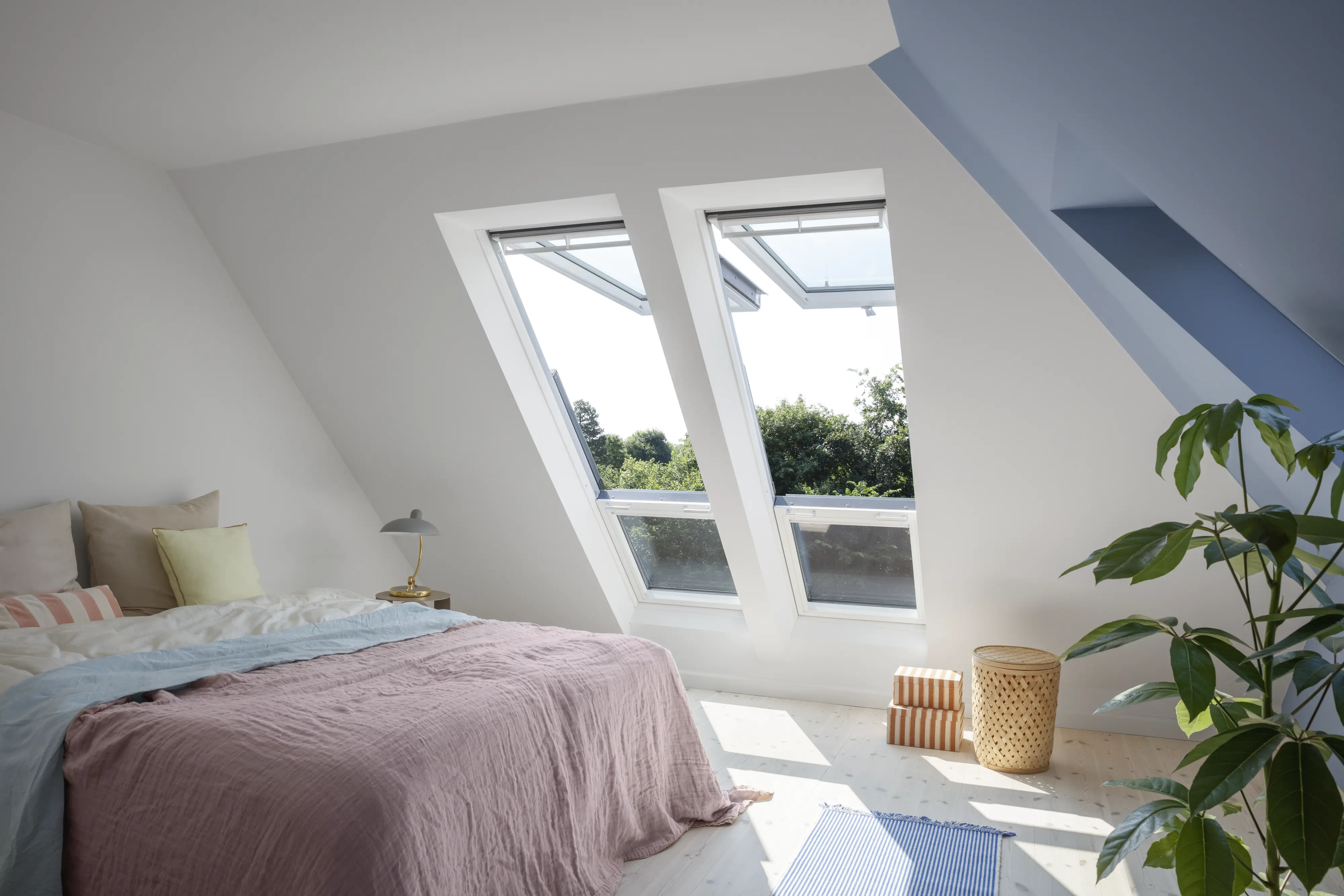 Attic bedroom with sloped ceiling and open VELUX roof windows, natural light.