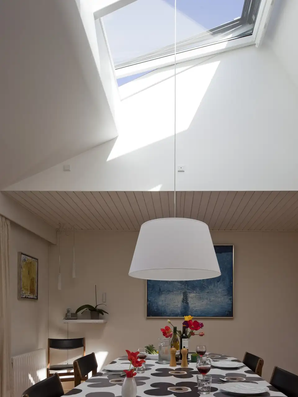 Sala da pranzo con finestra per tetti e lampada a sospensione bianca che illumina il tavolo