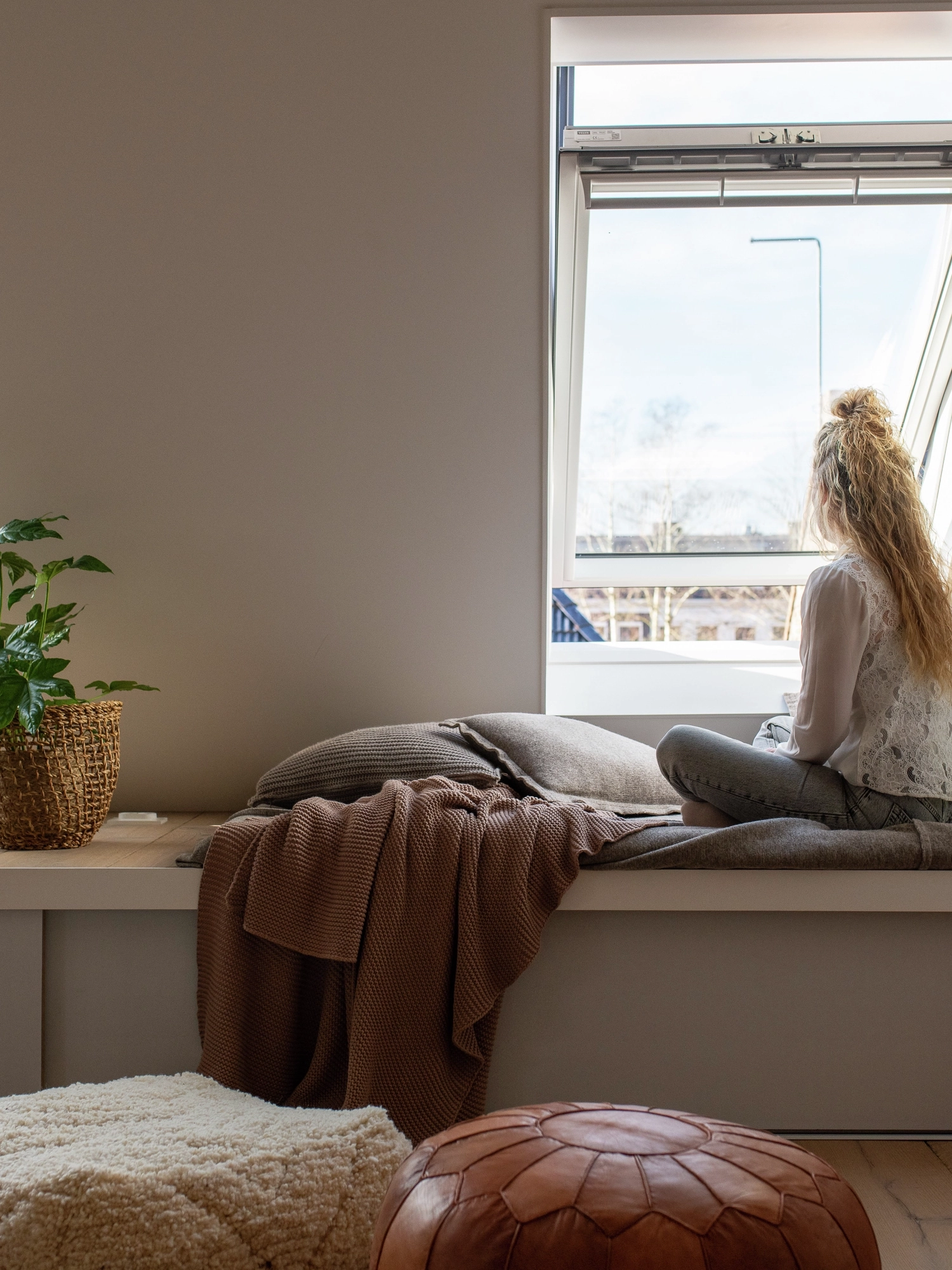 Vrouw die op een vensterbank zit en uit haar VELUX dakraam kijkt