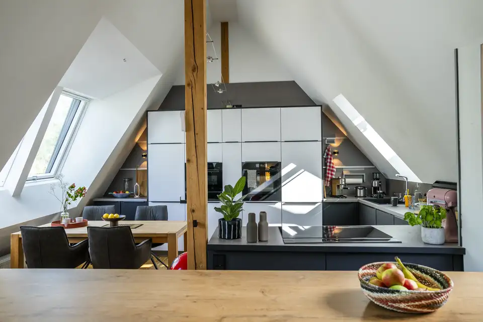 Cuisine avec fenêtres de toit sur les deux pans du toit et un mur vertical peint en gris foncé presque jusqu’au sommet. 