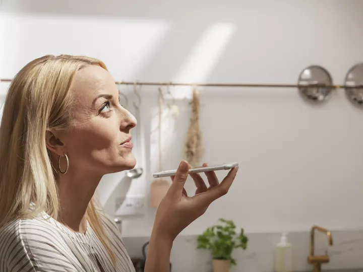 Frau spricht in ihr Smartphone und schaut zum Küchenfenster ihres Smarthauses | VELUX Magazin
