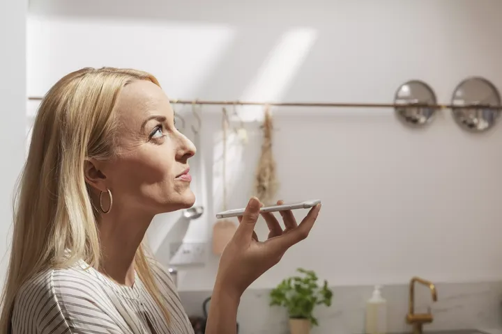 Frau spricht in ihr Smartphone und schaut zum Küchenfenster ihres Smarthauses | VELUX Magazin
