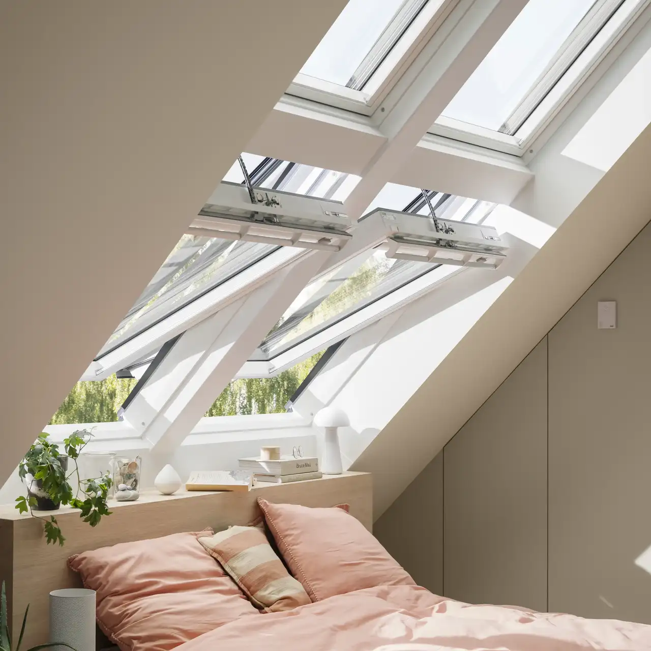 Chambre mansardée avec fenêtres de toit VELUX ouvertes sous un plafond incliné. 