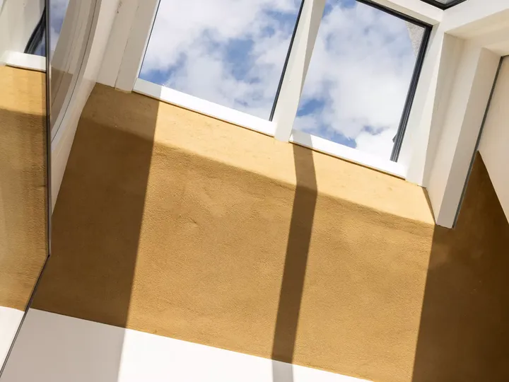 Innenansicht eines VELUX Dachflächenfensters mit blauem Himmel und Sonnenlicht, das Schatten an die Wand wirft.