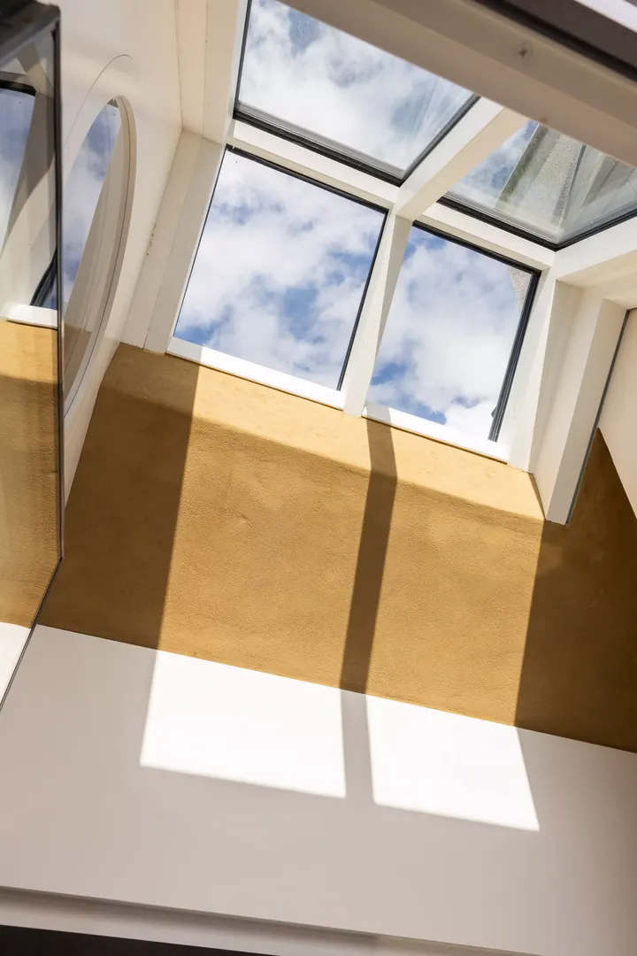 Innenansicht eines VELUX Dachflächenfensters mit blauem Himmel und dynamischen Schatten an der Wand.