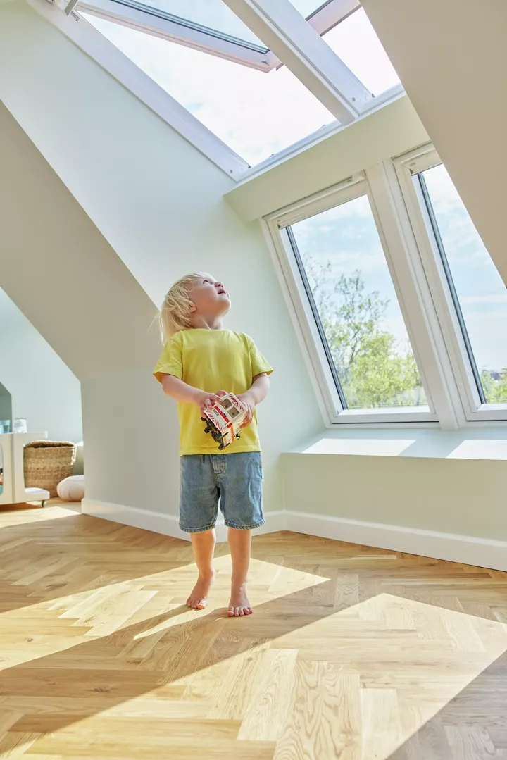 Kleiner Junge in Sommerkleidung schaut zu Dachfenster-Kindersicherung mit Sicherheitsgriff auf | VELUX Magazin