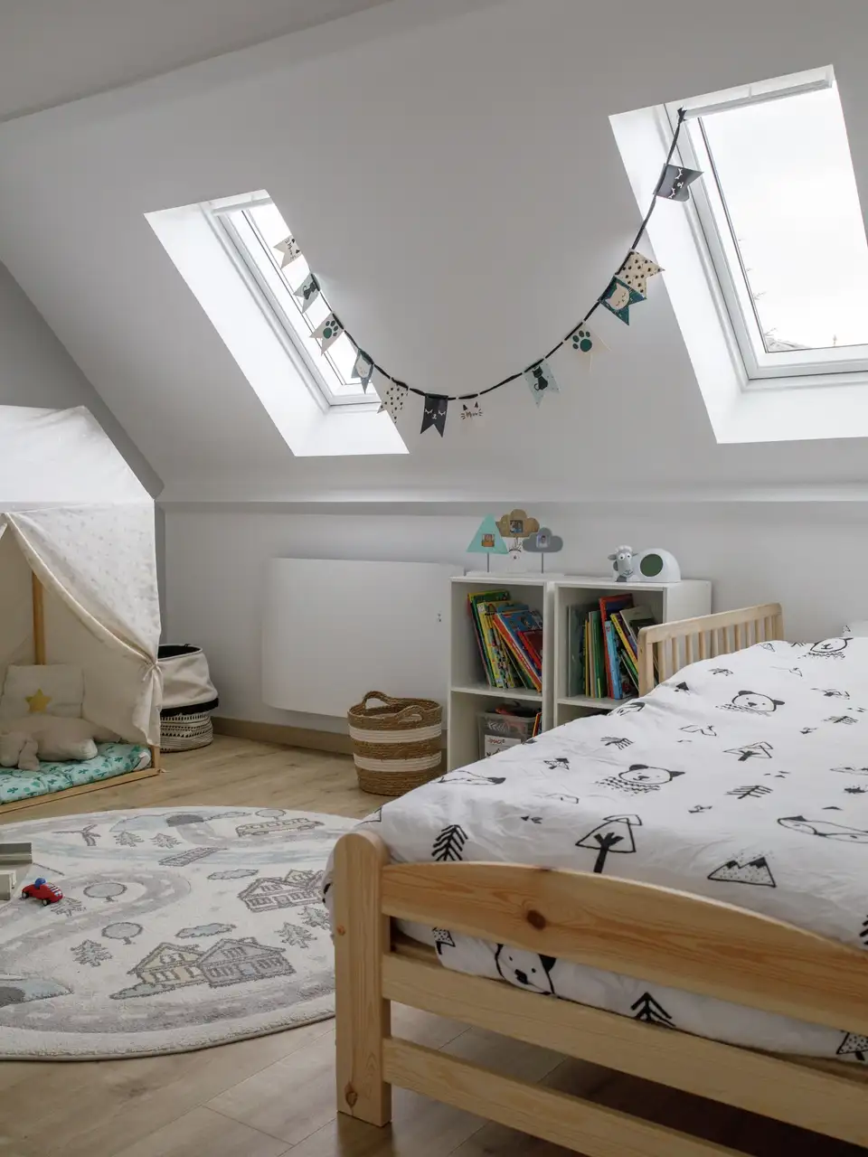 Chambre d’enfant aménagée sous combles avec deux fenêtres de toit. 