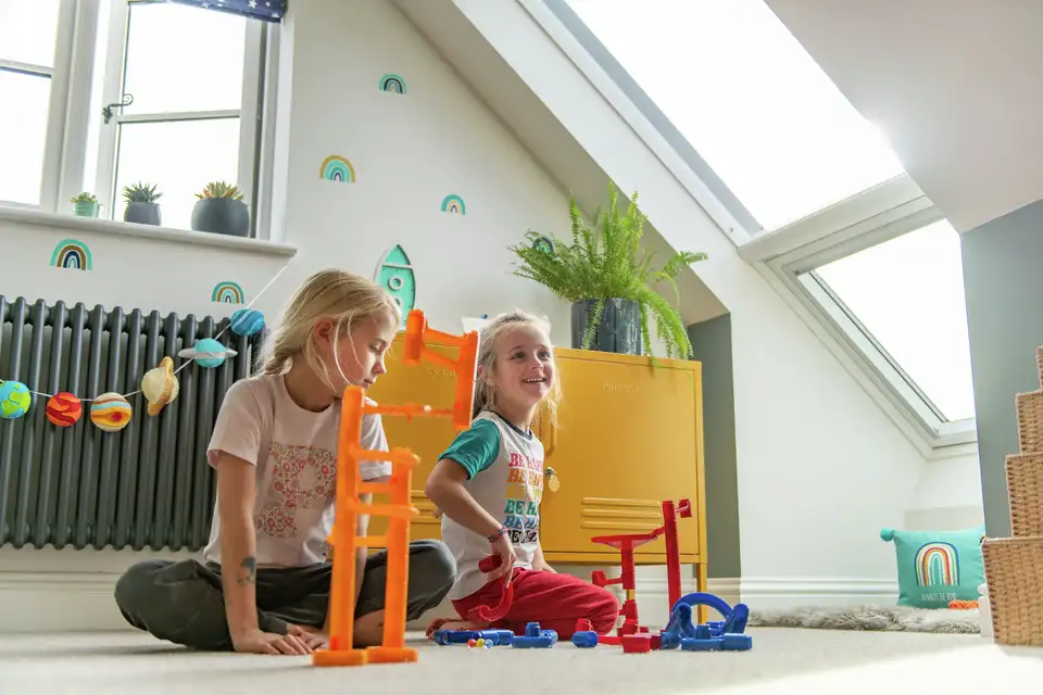 Twee kleine meisjes spelen op een zolderkamer die baadt in het daglicht dankzij de VELUX dakramen. 