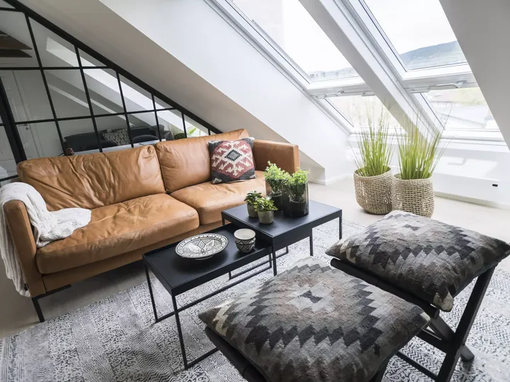 Stilvolles Wohnzimmer im Dachboden mit VELUX Dachflächenfenster, Ledersofa und grünen Pflanzen.