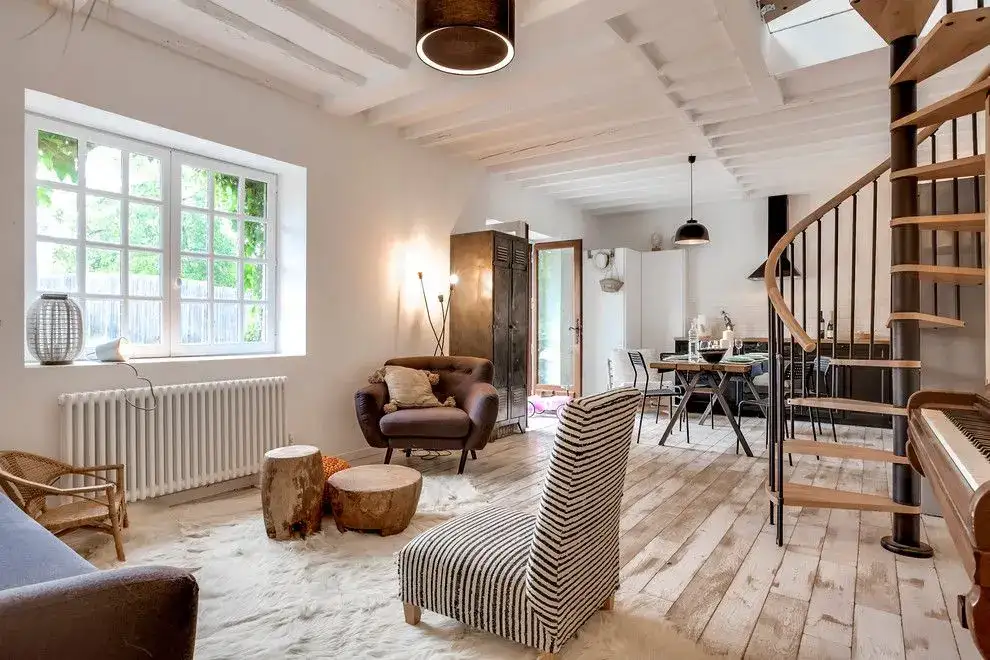 Séjour ouvert sur une cuisine avec escalier en colimaçon et éclairé par des fenêtres de toit installées à l’étage.