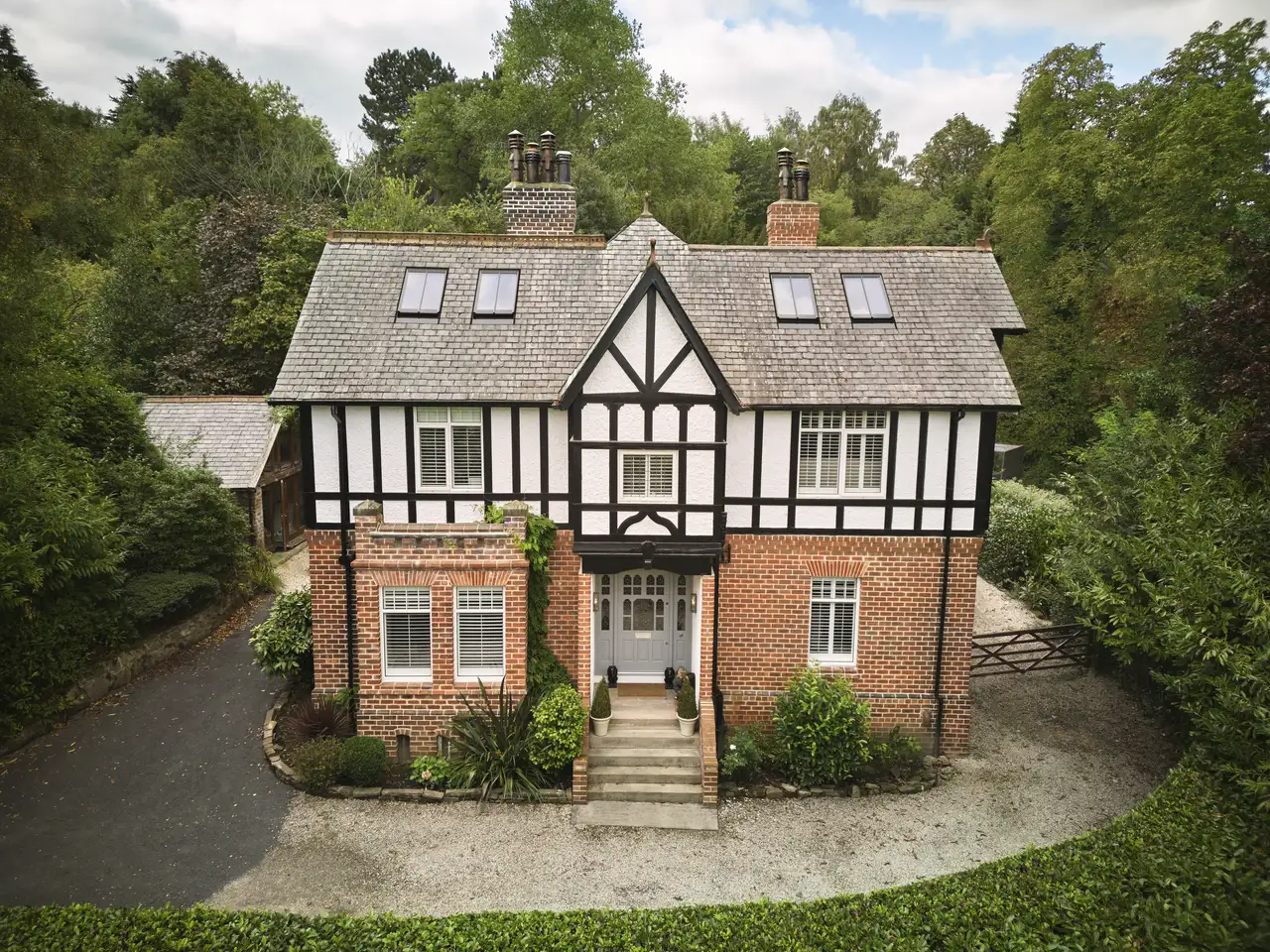 Red brick house with slate roof and bay windows, surrounded by a garden