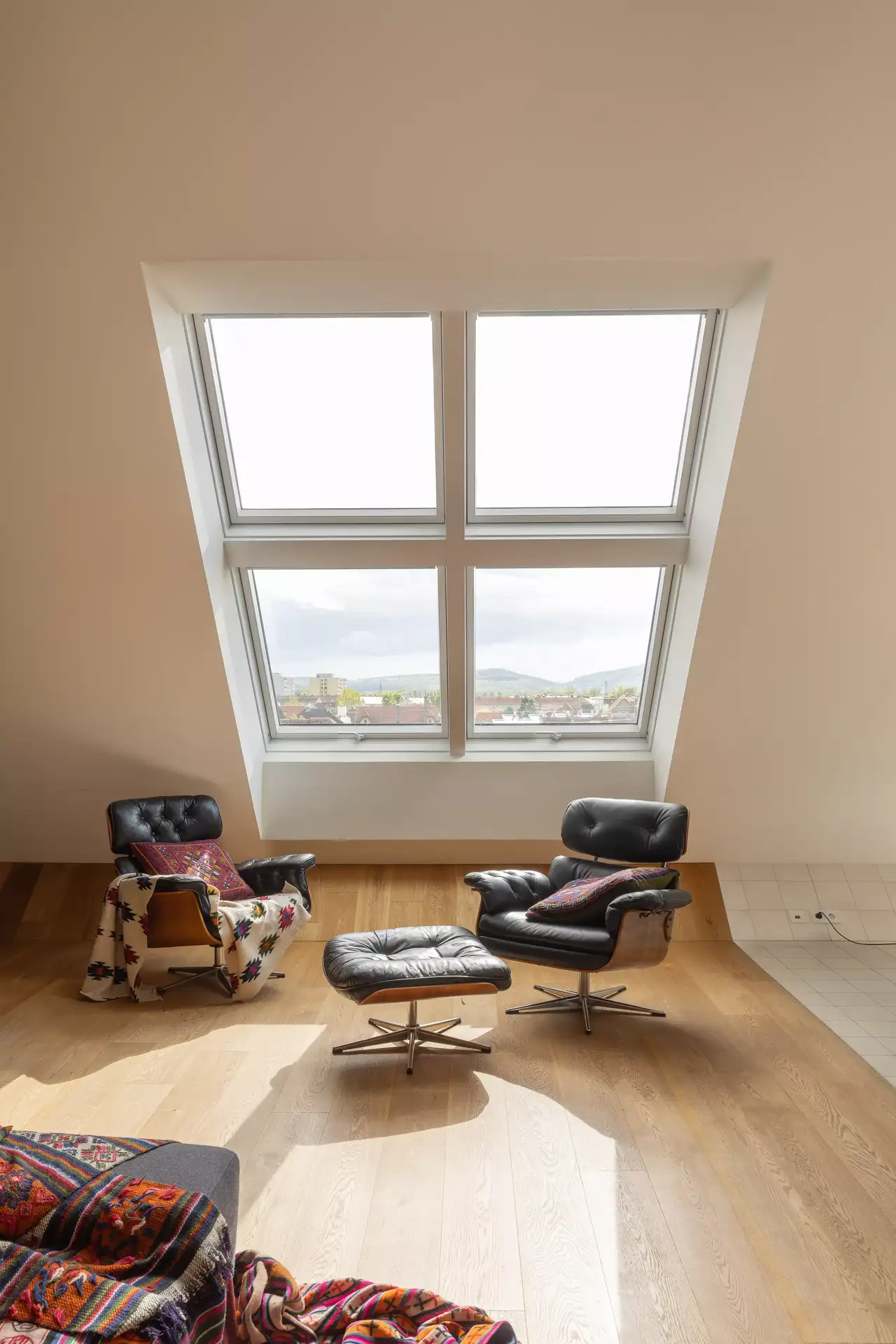 Gemütliches Wohnzimmer im Dachboden mit Sofa und VELUX Dachflächenfenster, die Sonnenlicht hereinlassen.