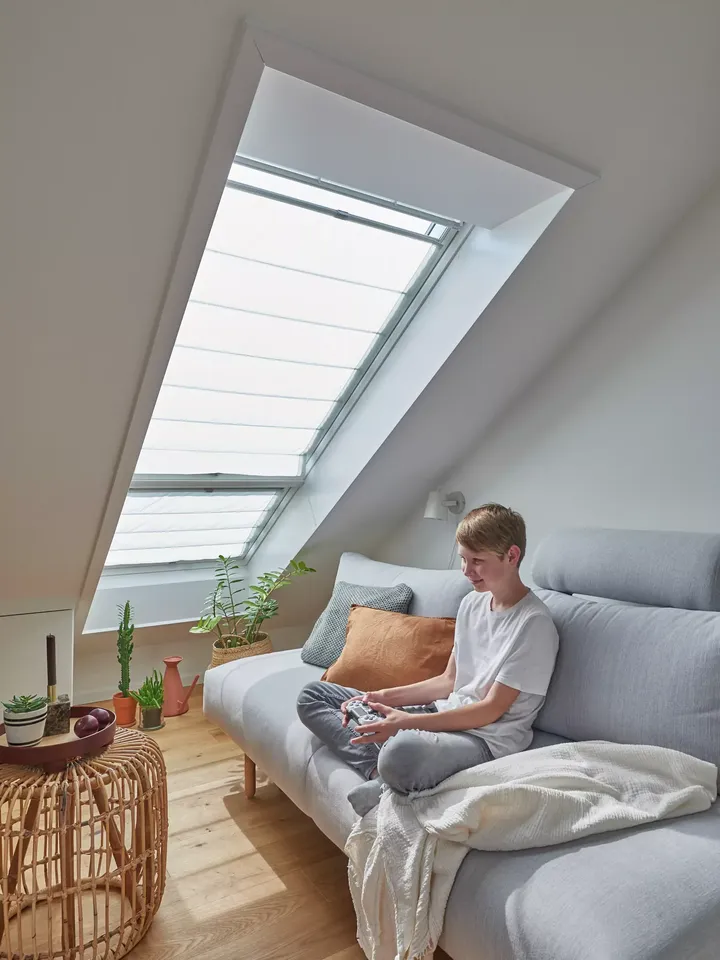 Dachboden-Wohnzimmer mit grauem Sofa, Pflanzen, hölzernem Boden und VELUX Dachflächenfenster.