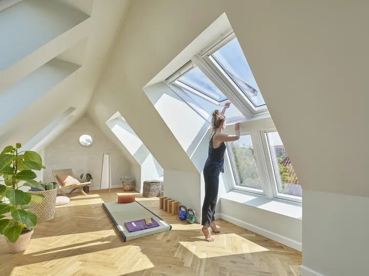 Frau in Yogakleidung öffnet das Dachfenster ihres offenen Spitzbodens | VELUX Magazin