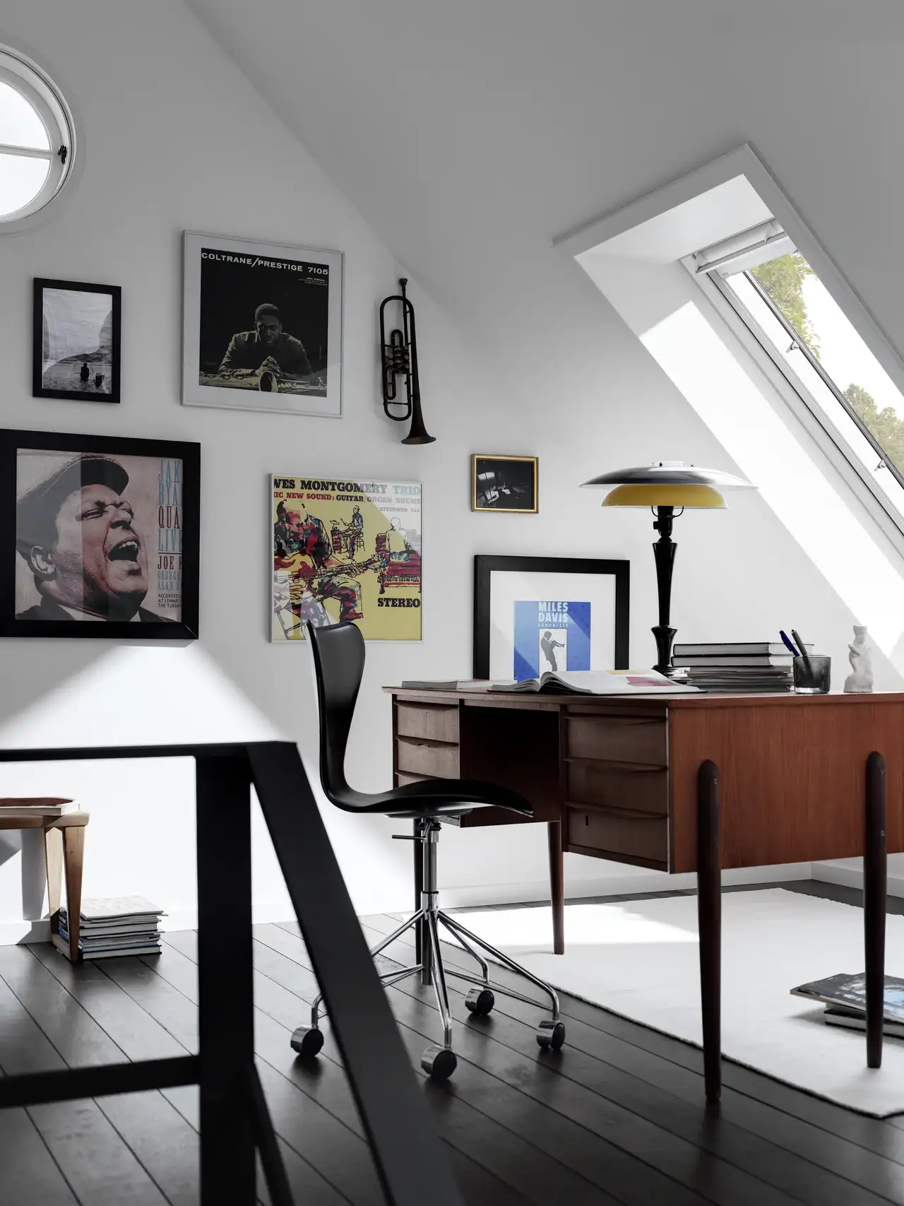 Bureau en mansarde avec bureau en bois, fenêtre de toit et mur décoré de posters et photographies.