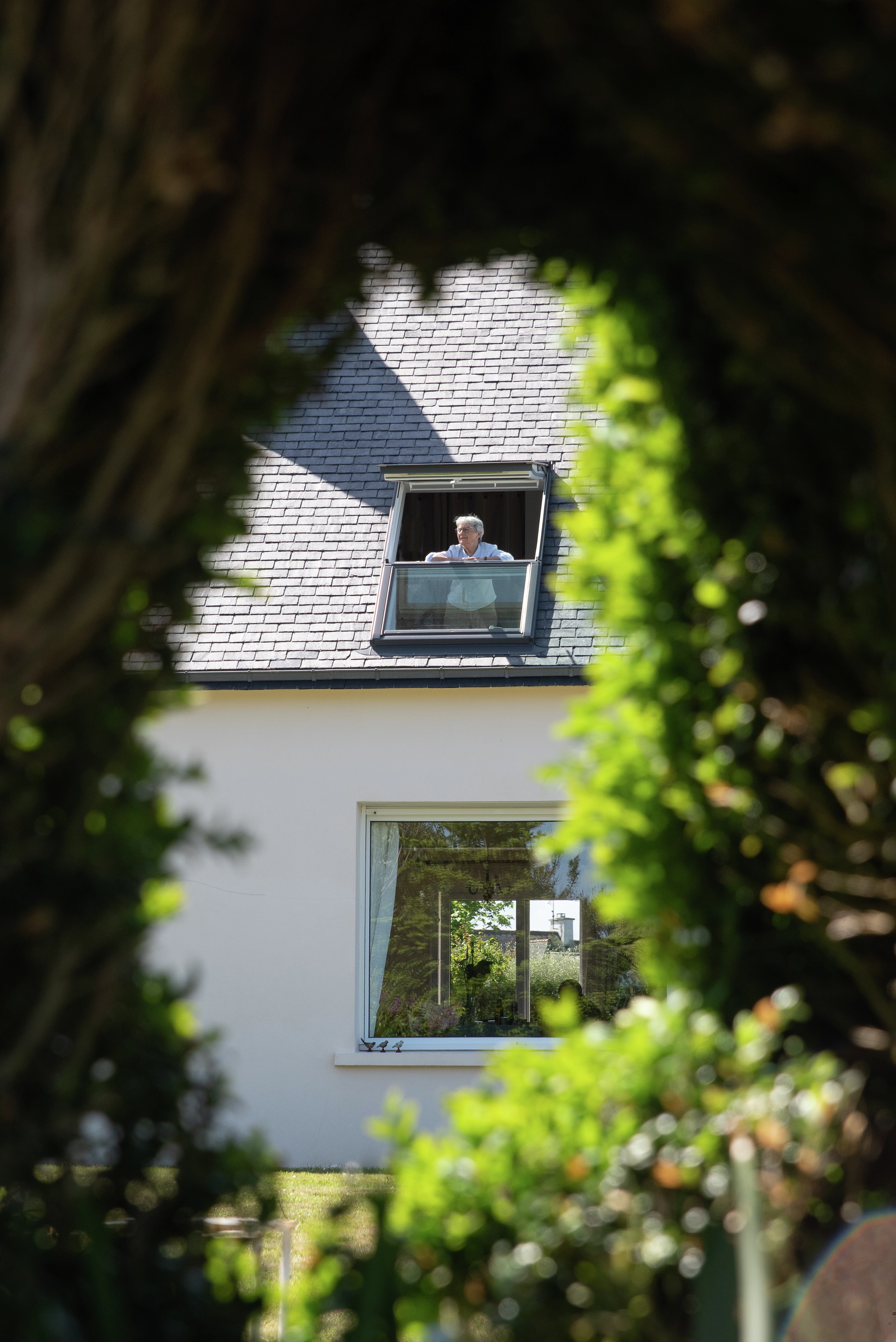 Femme regardant par la fenêtre du balcon de sa maison de campagne vue du jardin.