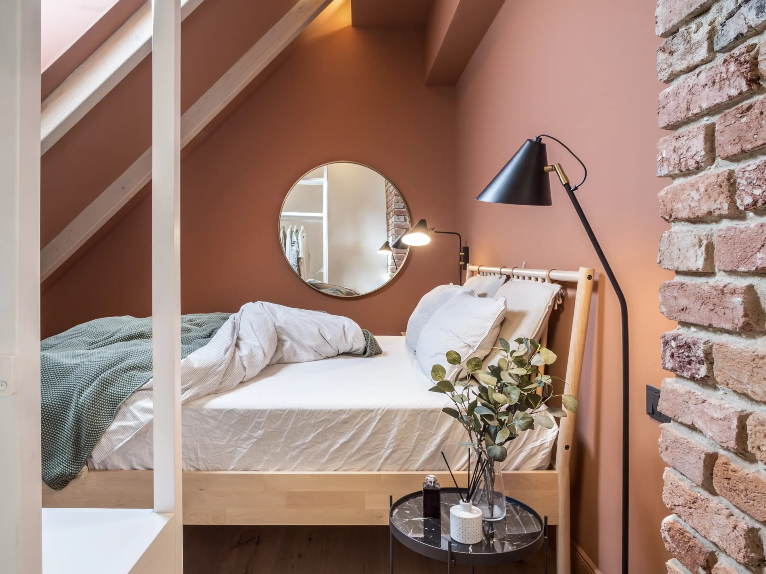 Une chambre douillette et bien éclairée avec un lit confortable, des murs en briques apparentes et une fenêtre Velux qui laisse entrer une lumière naturelle abondante.