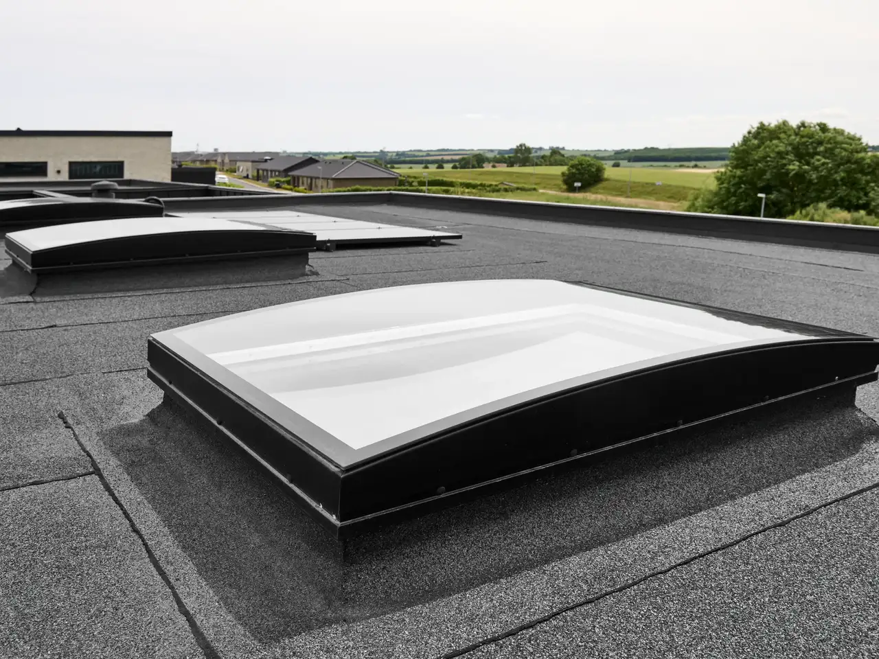 Finestre per tetti piani VELUX con vetro curvo installate su un tetto piano di una casa circondata dalla natura