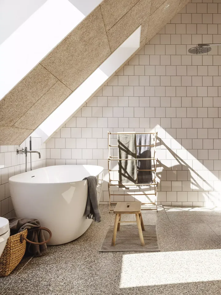 Modernes Badezimmer mit VELUX Dachflächenfenster, freistehender Badewanne und weißen Fliesen.