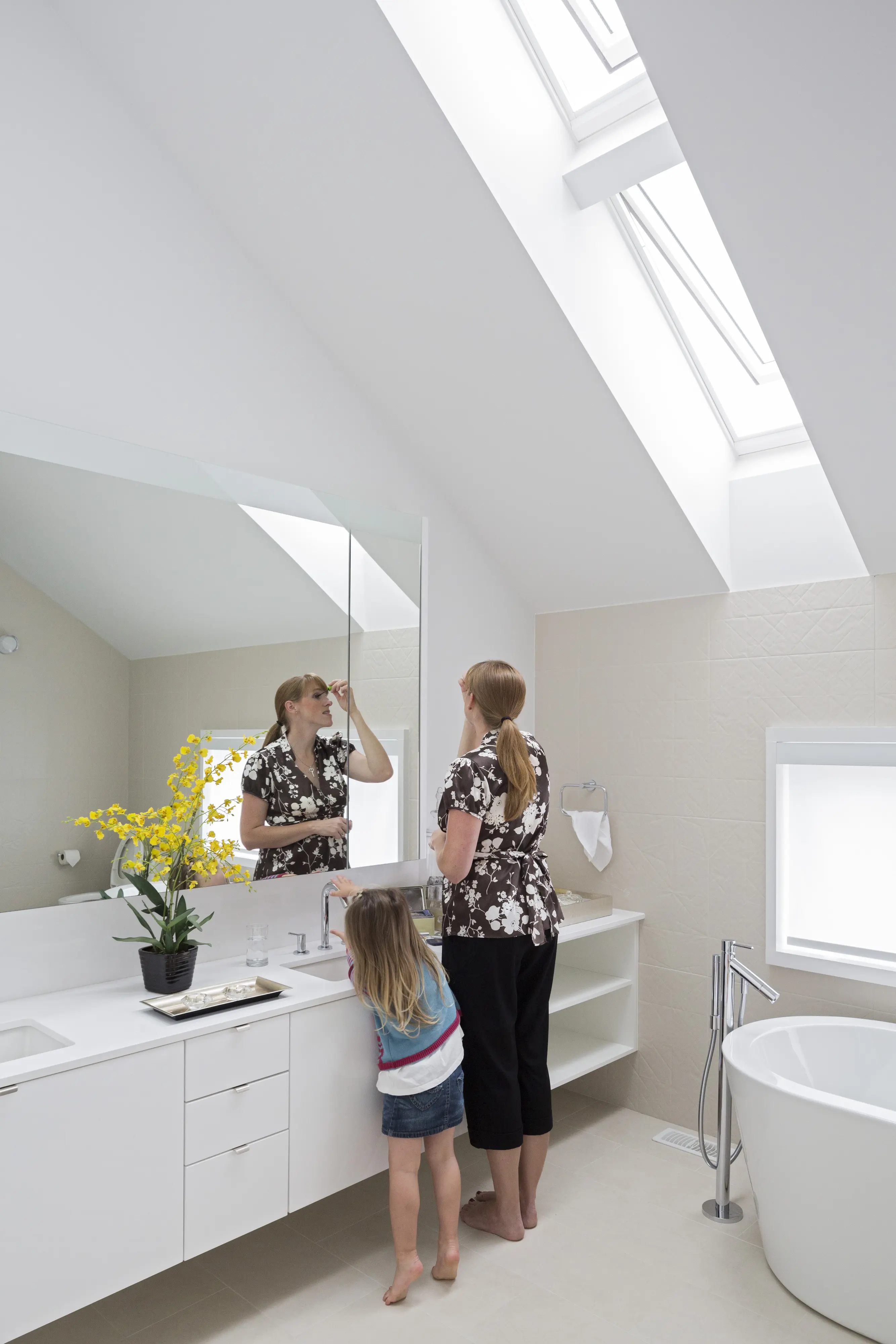 Baie modernă cu tavan înclinat și ferestre de mansardă VELUX, mamă și copil prezenți.