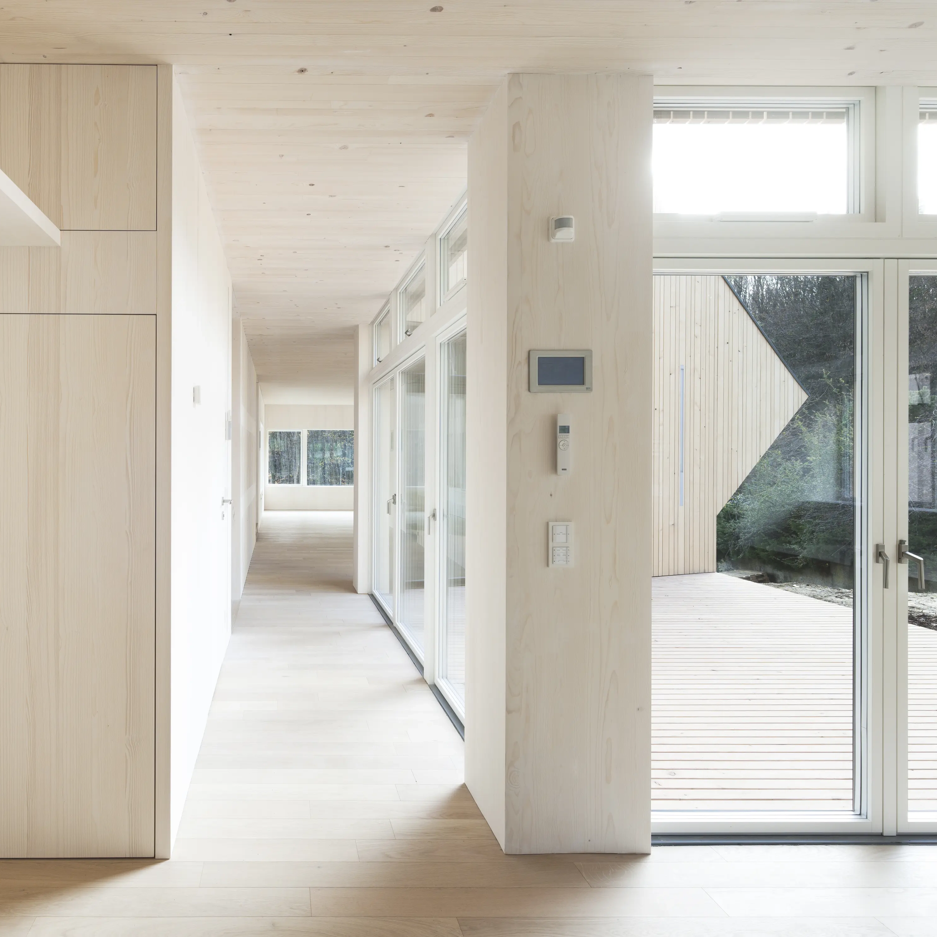 Modern corridor with large glass windows and light wood flooring.