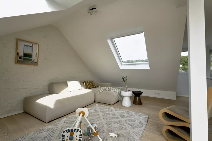 Gemütliches Dachboden-Wohnzimmer mit VELUX-Fenster, Sofa, Spielzeug und modern-rustikaler Dekoration.