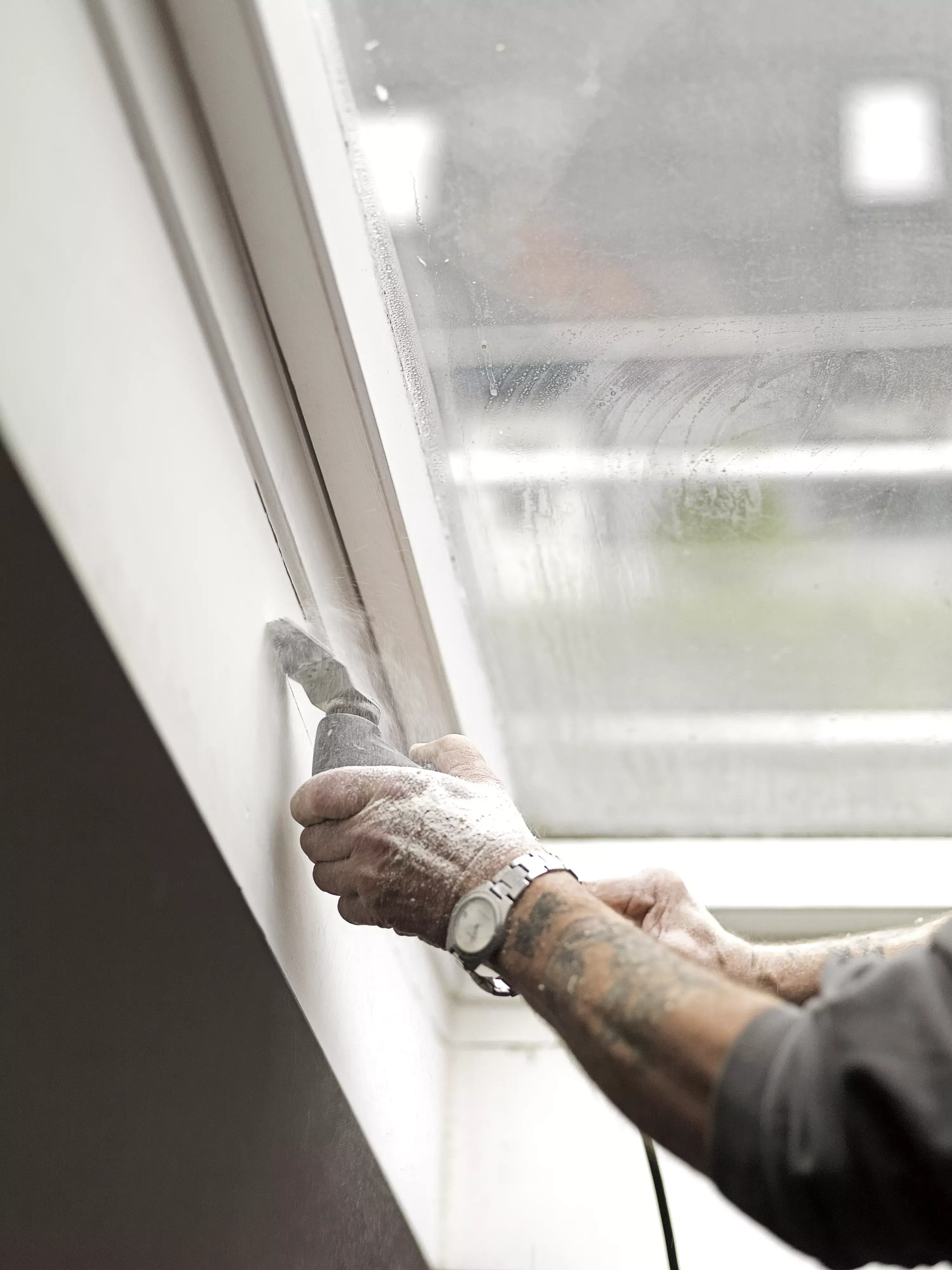 Une main applique du mastic pour sceller le bord d’une fenêtre Velux, illustrant une tâche d’entretien courante pour améliorer l’isolation et prévenir les fuites.