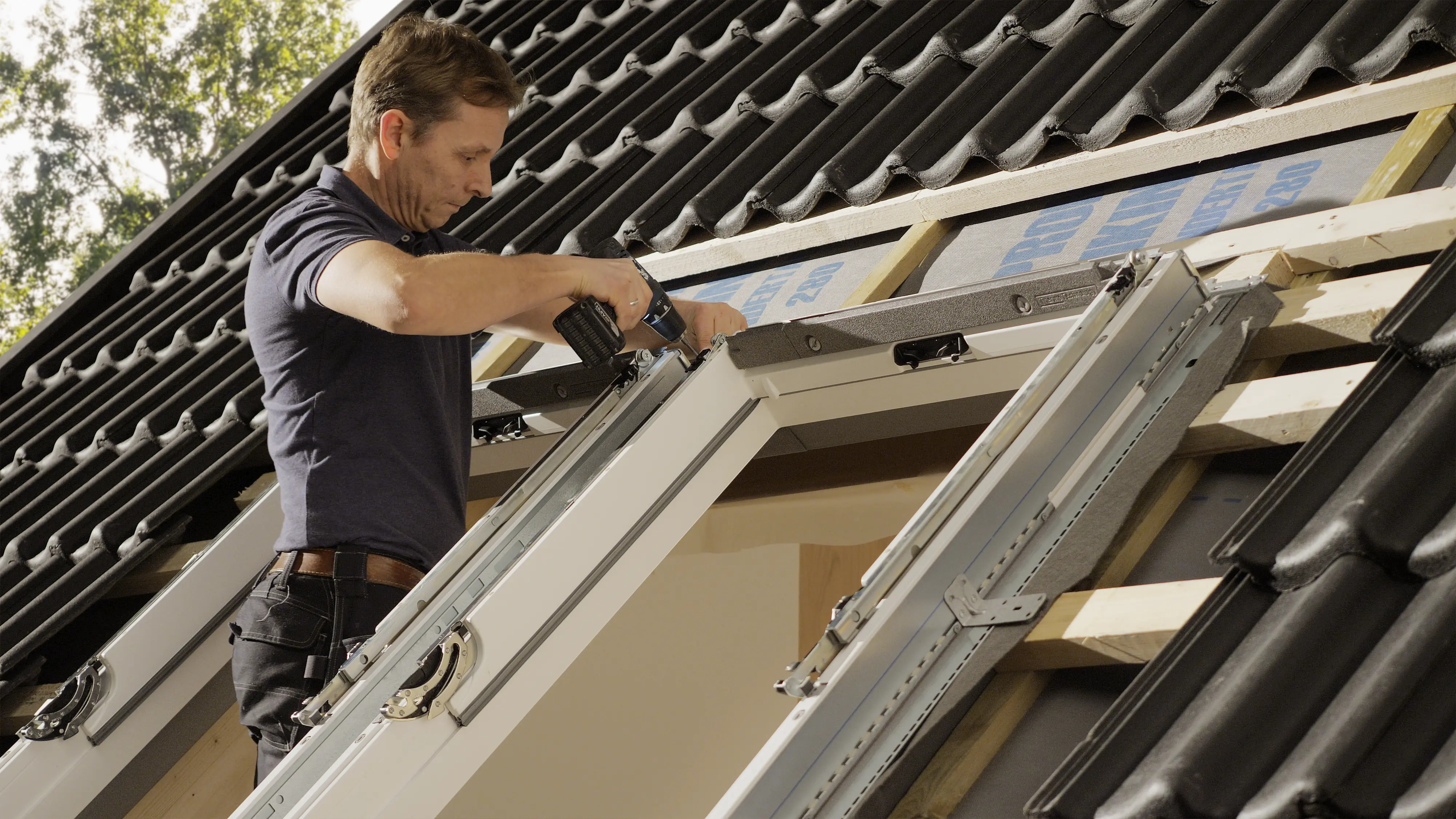 Worker installing VELUX roof window on a tiled roof.