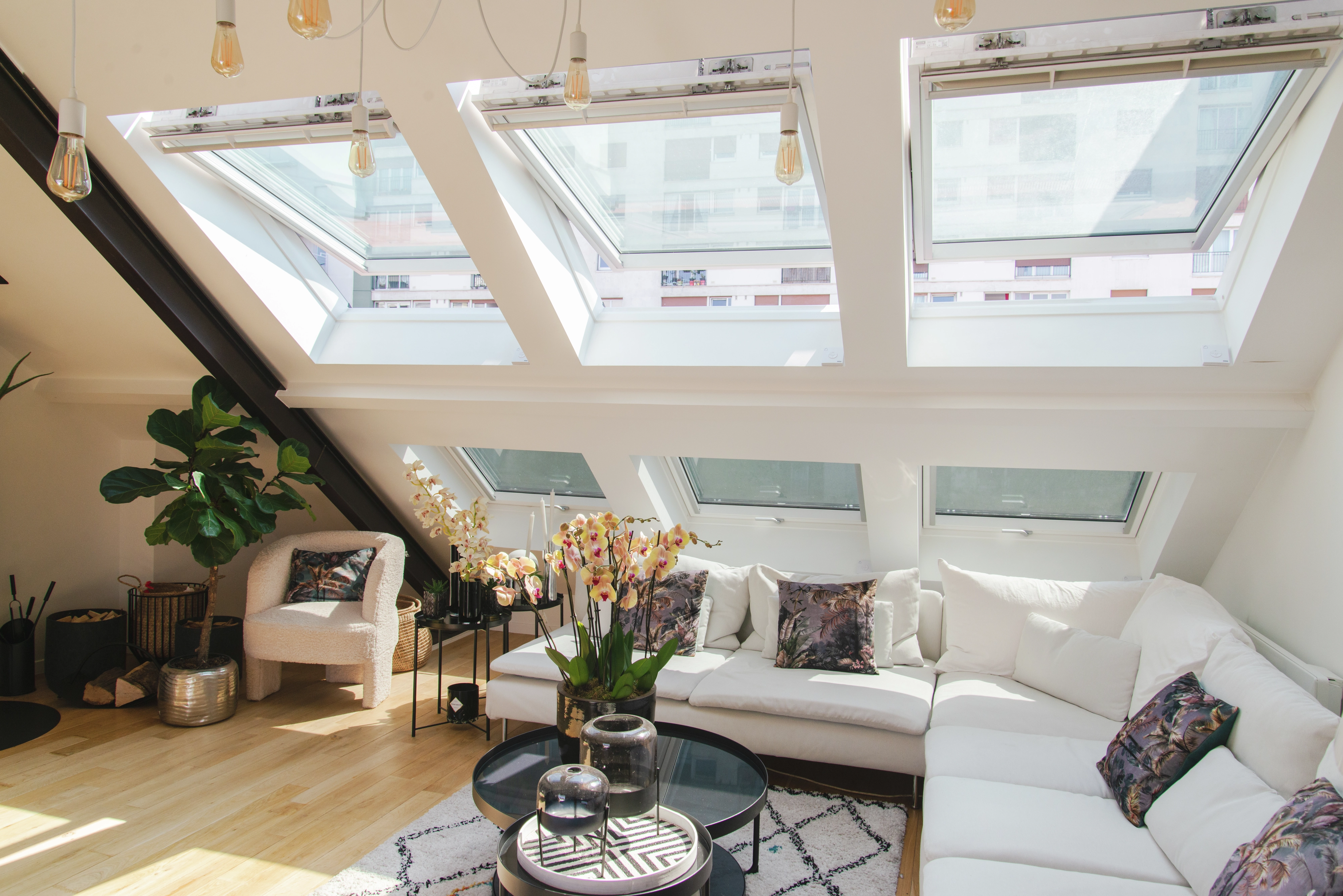 Salon de comble confortable avec lumière naturelle provenant des fenêtres de toit VELUX, canapé blanc et plantes.