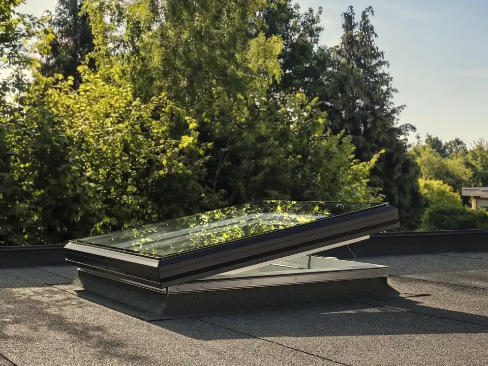 Electric VELUX flat rooflight open for ventilation on felt flat roof — low profile rooflight design in summer sun. 