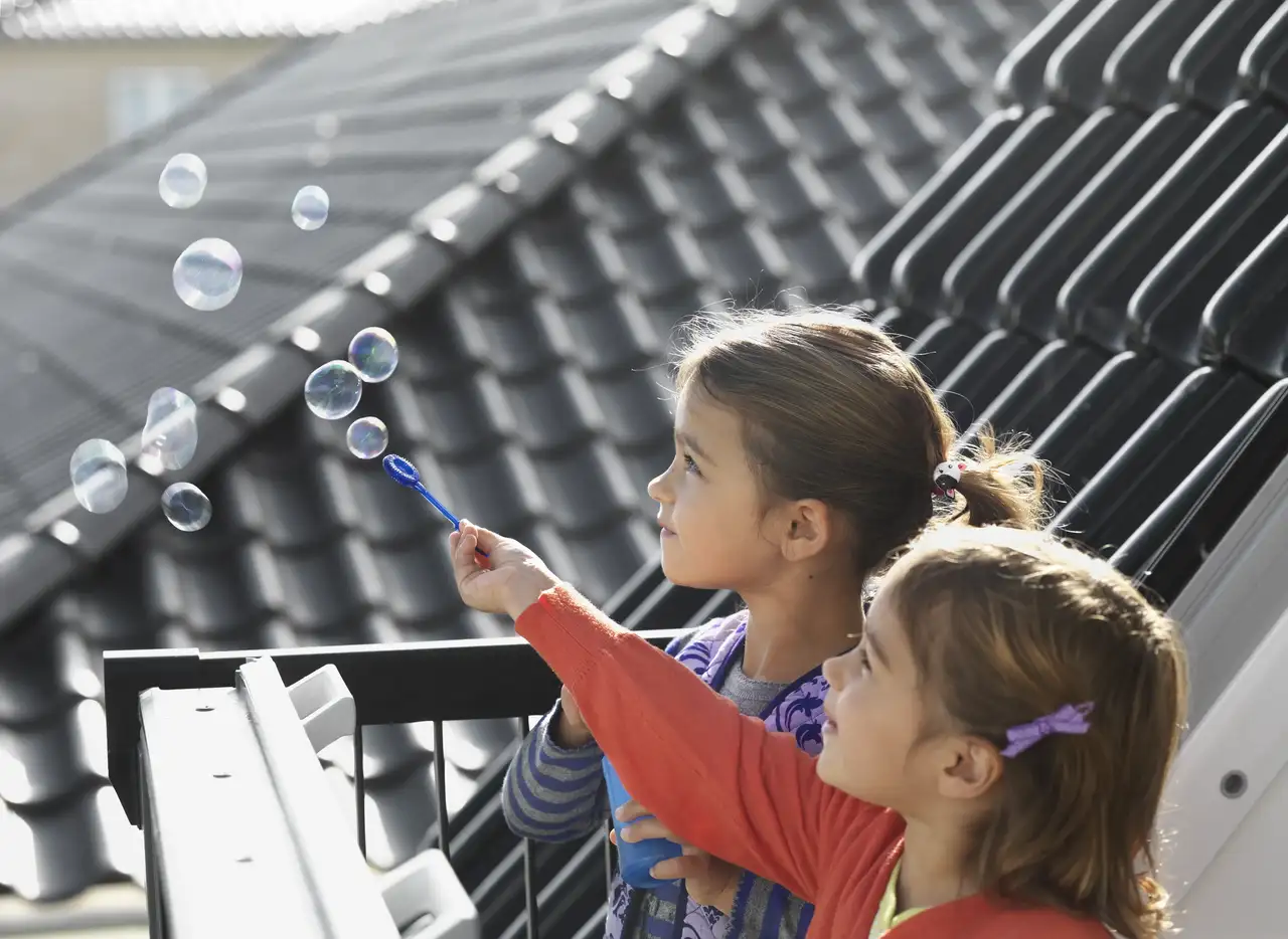Deux enfants jouent sur le balcon et font des bulles. Un enfant semble souffler des bulles, qui sont visibles dans l'air.