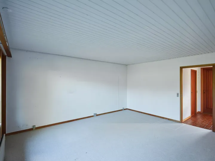 Heller und luftiger leerer Raum mit weißen Wänden, grauem Teppich und hölzerner Tür.