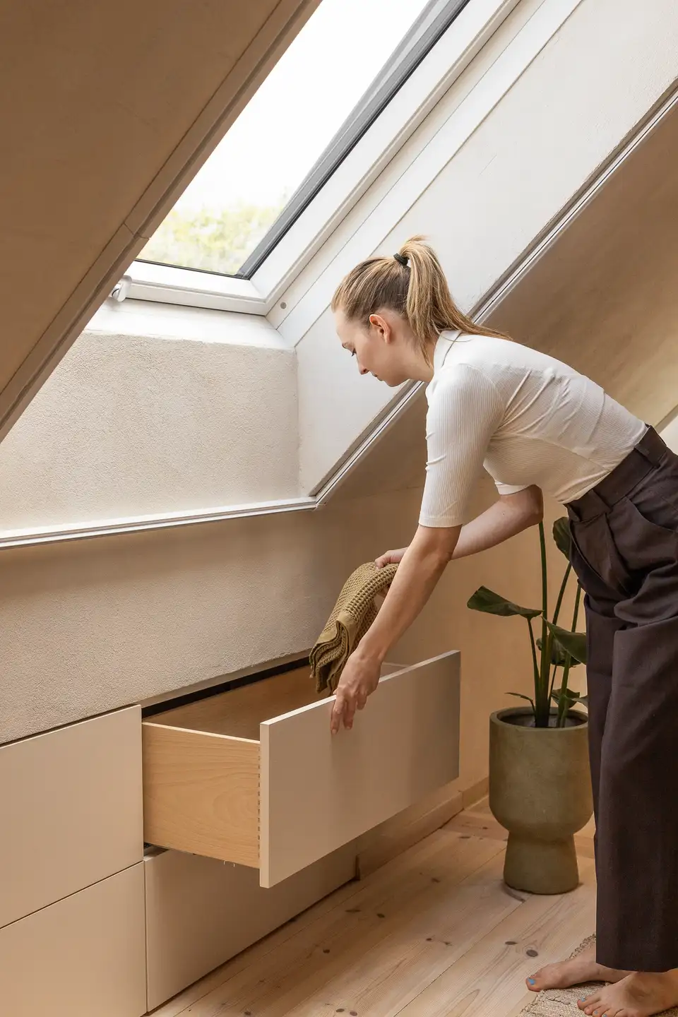Žena organizujúca zásuvku postavenú pod šikmou stenou, pod strešným oknom, s dôrazom na efektívne využitie priestoru v podkroví. | VELUX