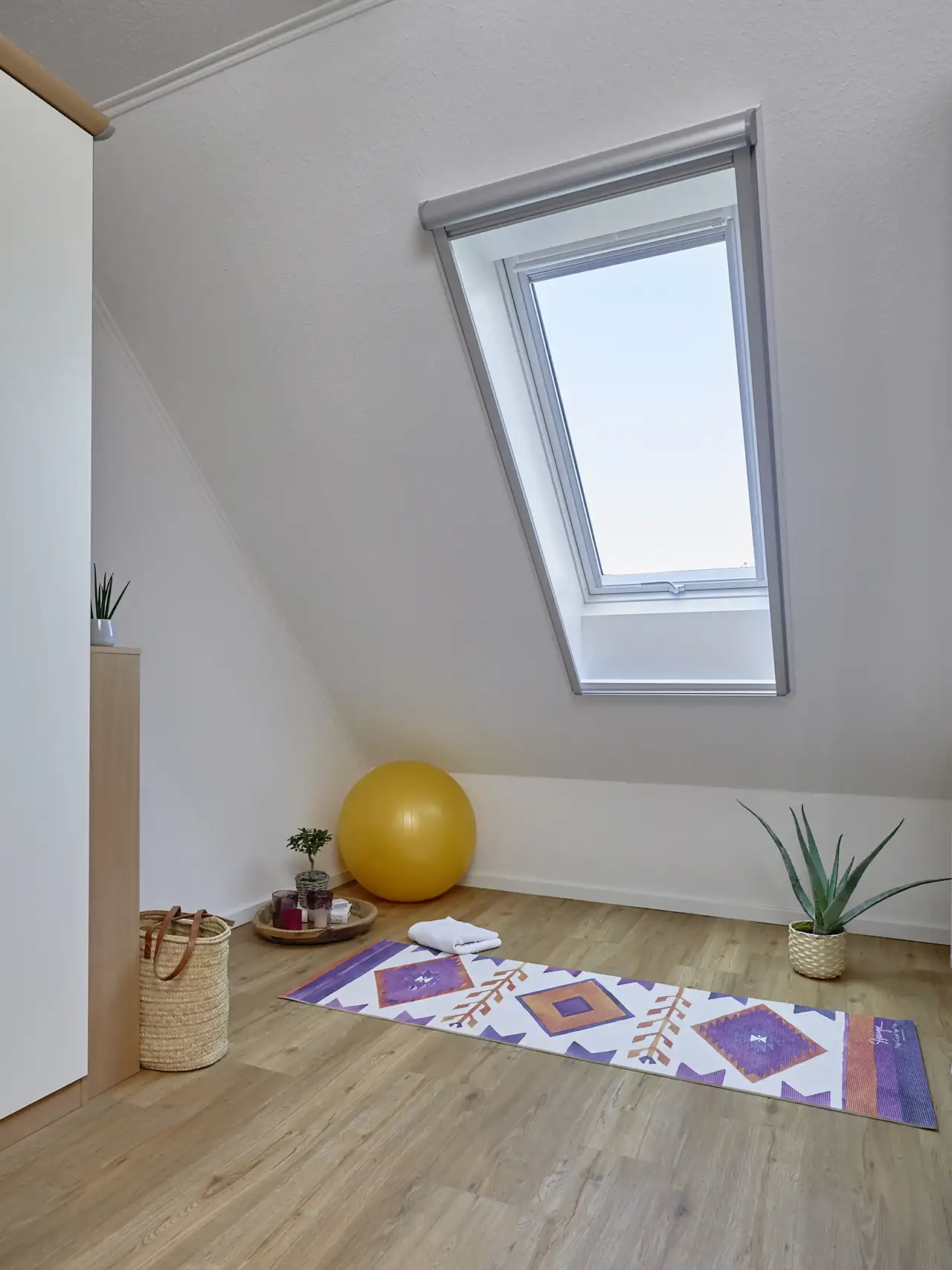 Coin méditation sous combles avec tapis de yoga, plantes vertes et lumière naturelle entrant par une fenêtre de toit VELUX. 