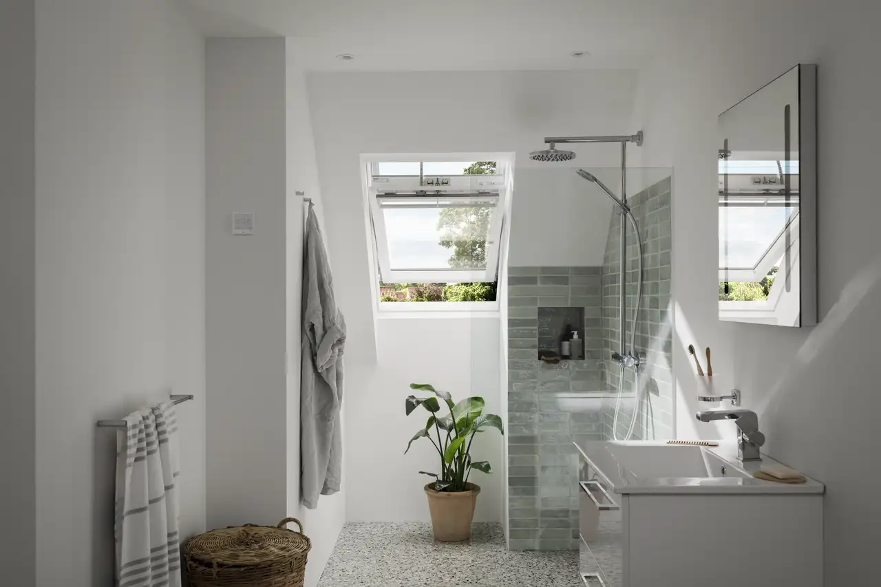 "Afbeelding van een moderne douchekamer met groene tegels, veel natuurlijk licht en een open VELUX dakvenster met uitzicht op de bomen.”