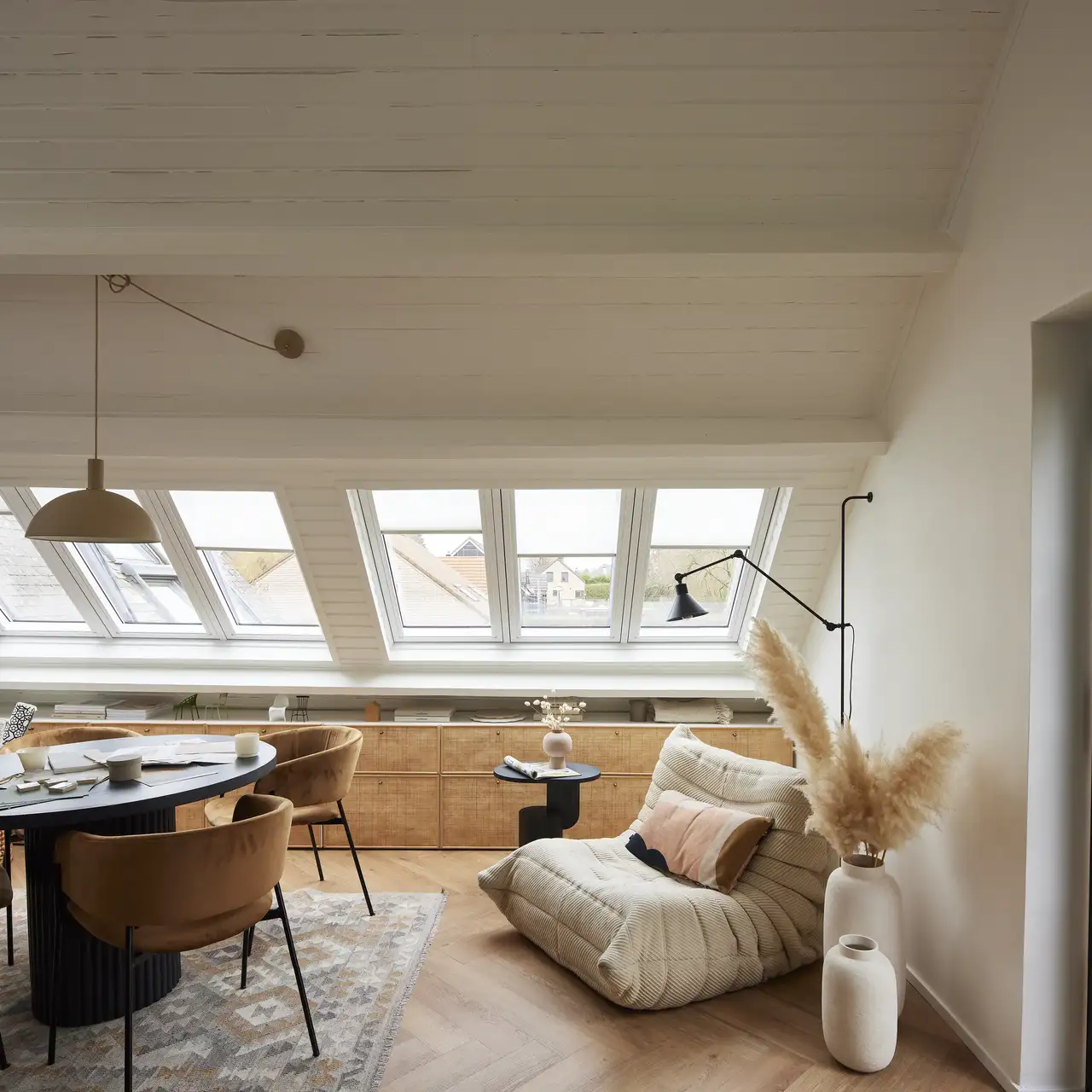 Espaço de convivência no sótão com teto inclinado e janelas de telhado VELUX, decoração acolhedora.