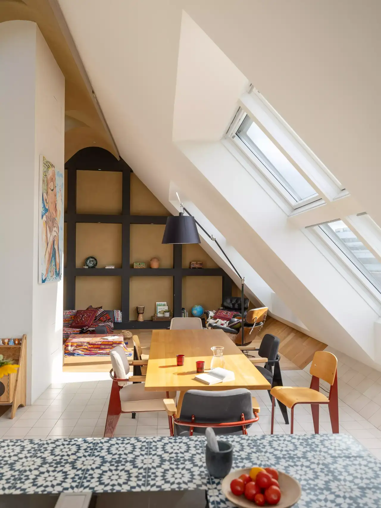 Dachboden-Esszimmer mit natürlichem Licht durch VELUX Dachflächenfenster, hölzerner Tisch und offene Regale.