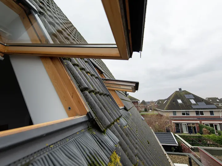 Nahaufnahme eines geöffneten VELUX Dachflächenfensters auf einem Ziegeldach mit Aussicht auf Vorstadthäuser.