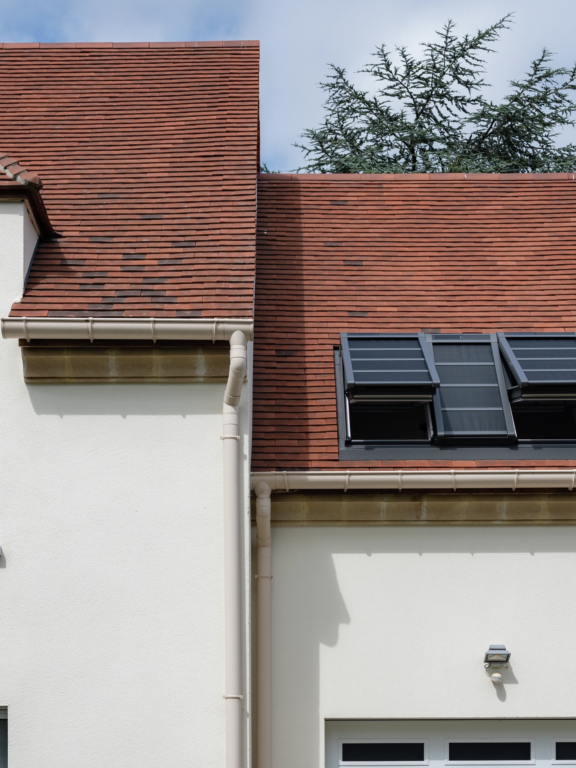 Haut des murs et toit d’une maison avec, d’un côté, une fenêtre verticale et, de l’autre, trois fenêtres de toit VELUX équipées de protections solaires extérieures.