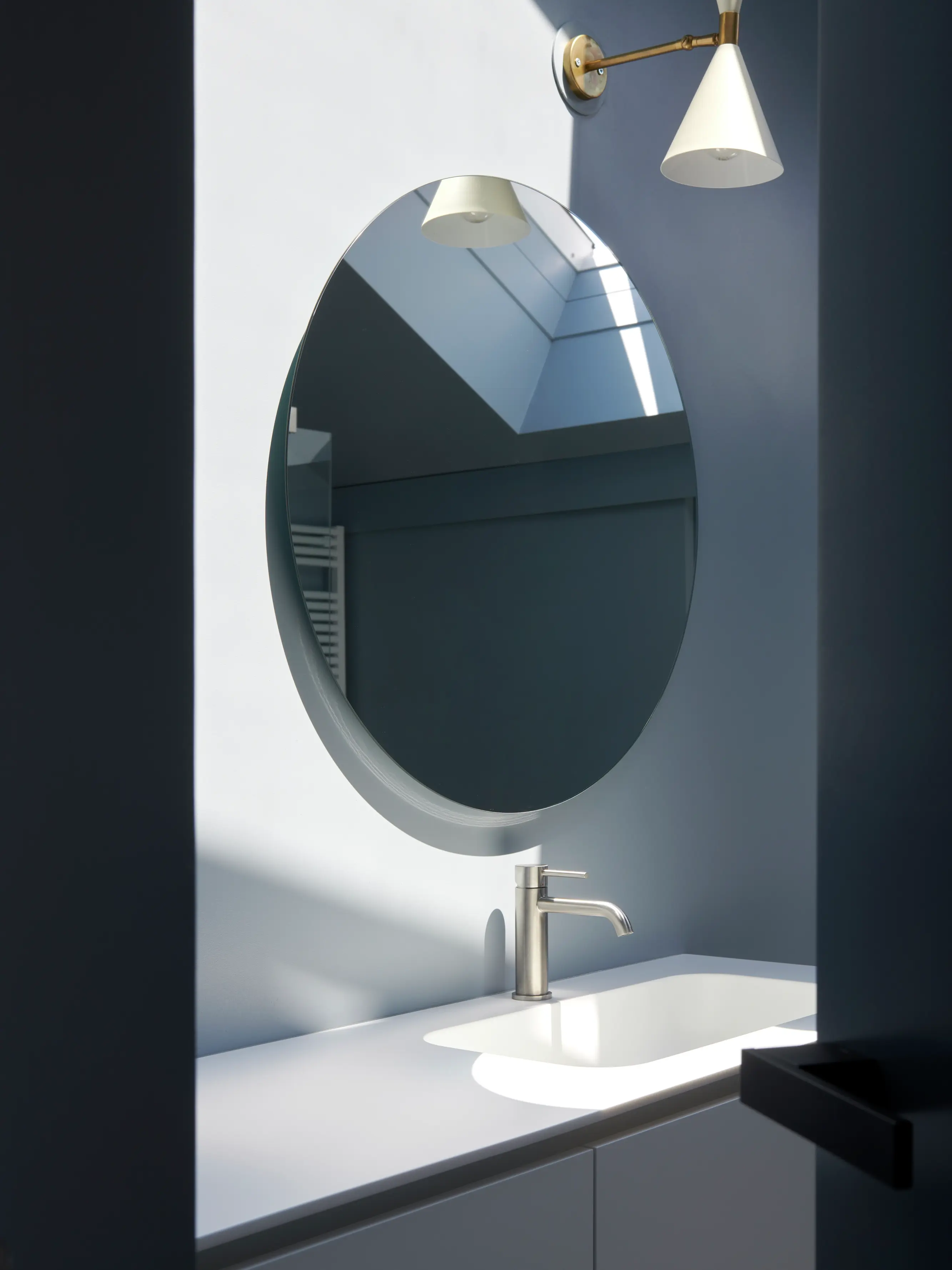 Miroir rond reflétant la lumière naturelle d'une fenêtre de toit VELUX dans une salle de bain moderne.